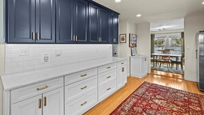 Una cucina con mobili blu scuro, piani di lavoro bianchi e un tappeto rosso con motivi.