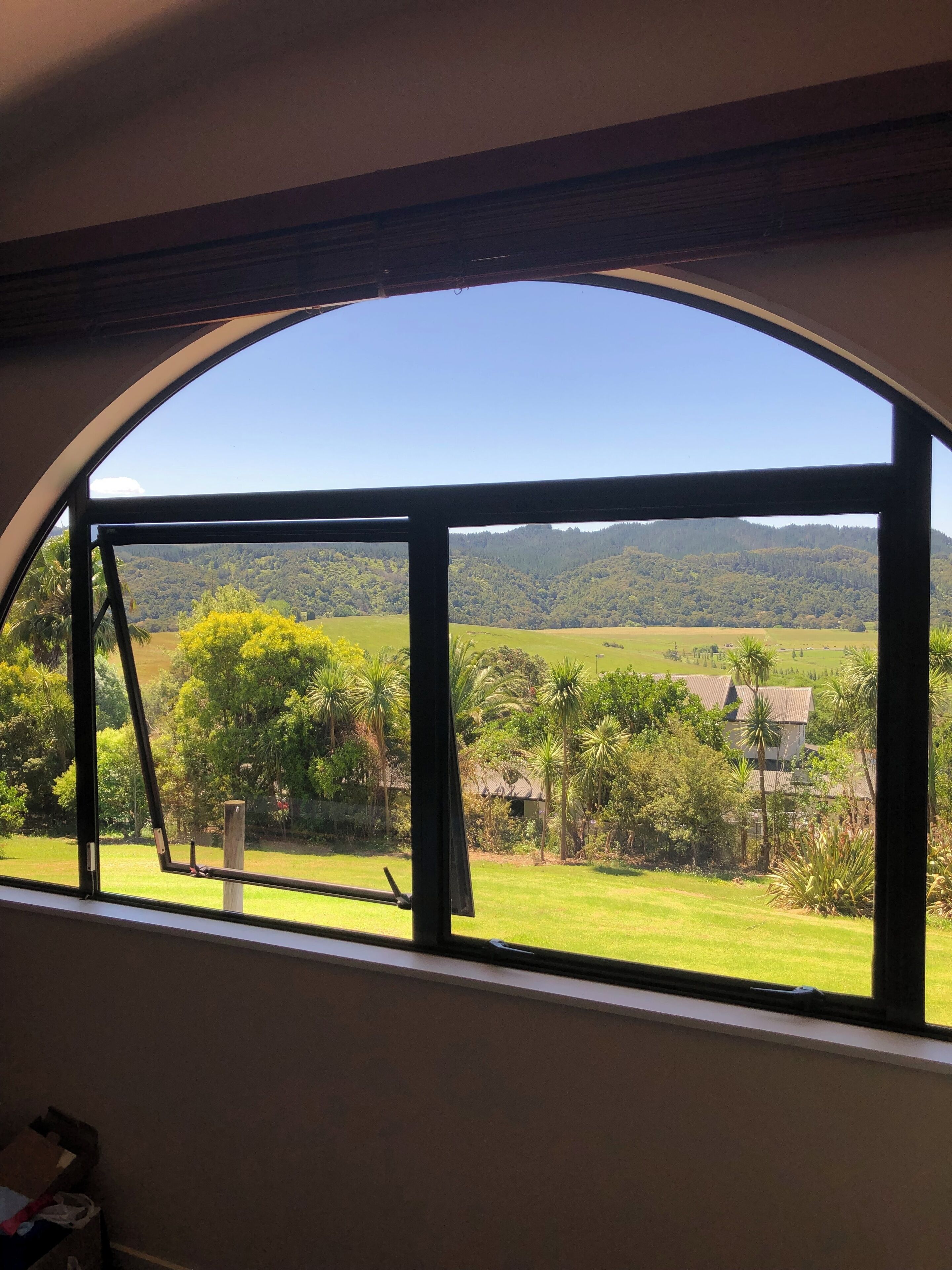 A room with a large arched window offering a view of a green landscape with trees and a hill in the distance.