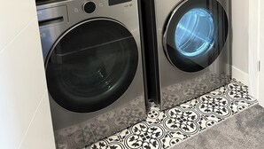 A laundry room with two front-loading washing machines, a shelf with wicker baskets, and a blue detergent container. - 
"Where the City Ends and the Mountains Begin." (Calgary)