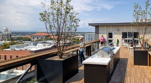 Eine Dachterrasse mit Grillbereich, Sitzgelegenheiten und Blick auf die Stadt.