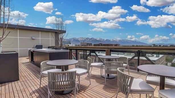 Een terras buiten met ronde tafels en stoelen, een barbecuehoek en uitzicht op bergen.