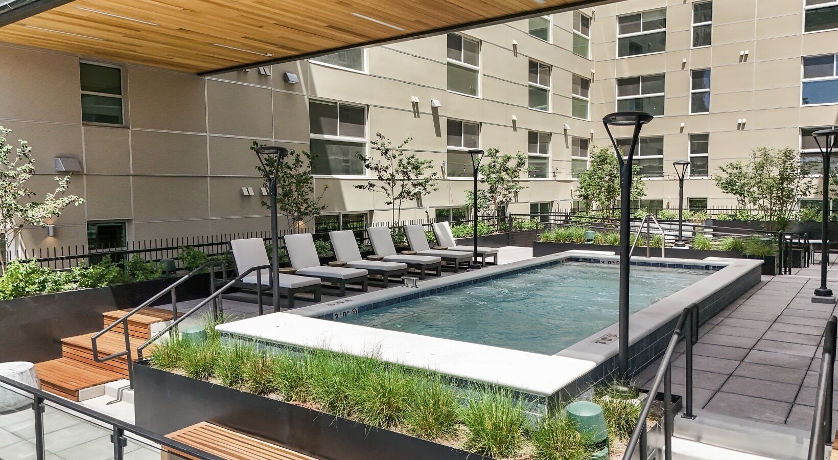 Un área de piscina en la azotea con sillones, una piscina pequeña y un edificio al fondo.