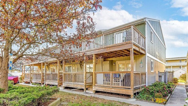 A two-story wooden house with a balcony, surrounded by a garden and a tree with autumn leaves. - Adorable 2-bedroom townhome with outdoor POOL in Ocean City (Ocean City)
