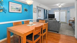 A dining area with a wooden table and chairs, a grey sofa, and a television in the background. - Adorable 2-bedroom townhome with outdoor POOL in Ocean City (Ocean City)