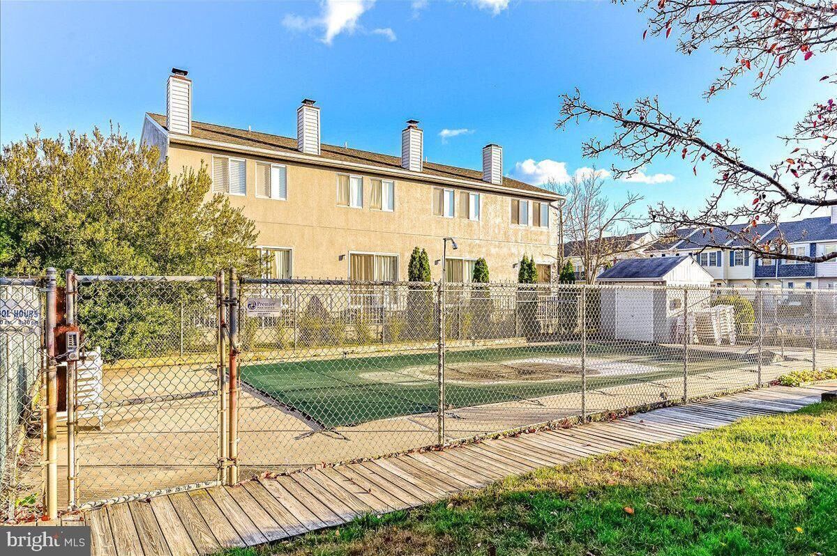 Patio trasero cercado con terraza de madera, cancha de tenis y un edificio con múltiples chimeneas.