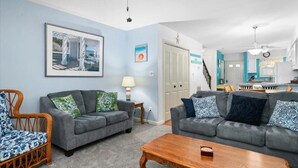 A living room with two grey sofas, a wooden coffee table, and a wicker chair. There is a framed picture on the wall and a lamp on a side table. - Adorable 2-bedroom townhome with outdoor POOL in Ocean City (Ocean City)