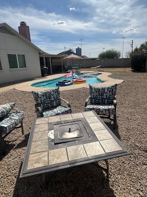 A backyard with a swimming pool, patio furniture, and a fire pit.
