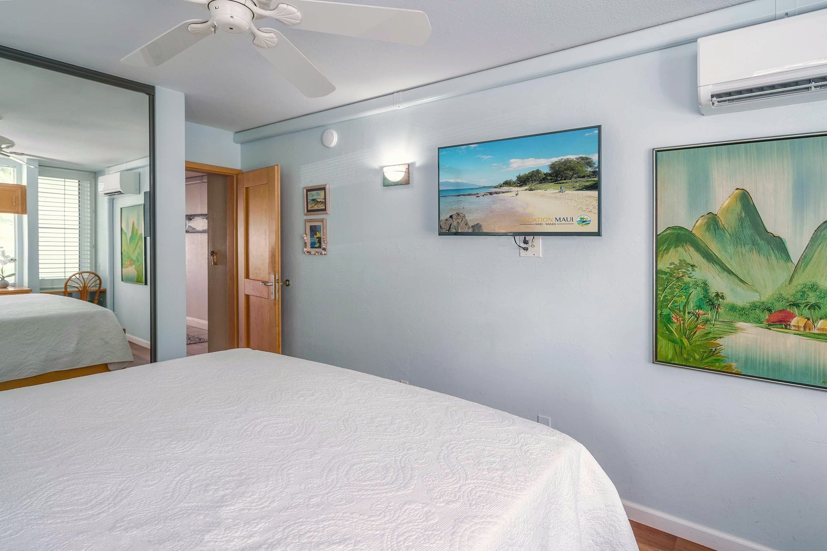A bedroom with a bed, a ceiling fan, a wall-mounted TV, and a painting.