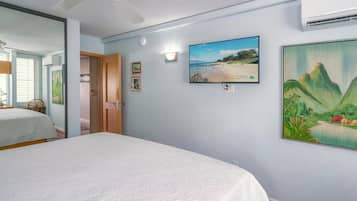 A bedroom with a bed, a ceiling fan, a wall-mounted TV, and a painting.