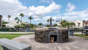 A barbecue area with a stone structure, a trash bin, and a bench. - Hale Kamaole 150 - Great Ocean Views From Private Lanai, No Carpet, Split AC! (Kihei)