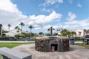 Área de churrasco com estrutura de pedra, lixeira e banco.