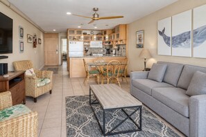 Ein modernes Wohnzimmer mit einem grauen Sofa, Korbstühlen, einem Holztisch und einem Fernseher.