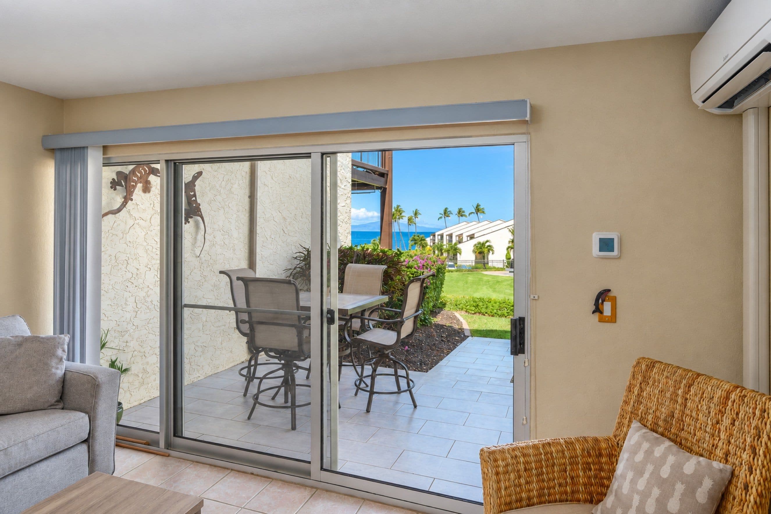 A hotel room with a sliding glass door leading to a balcony with outdoor seating and a view of the ocean.