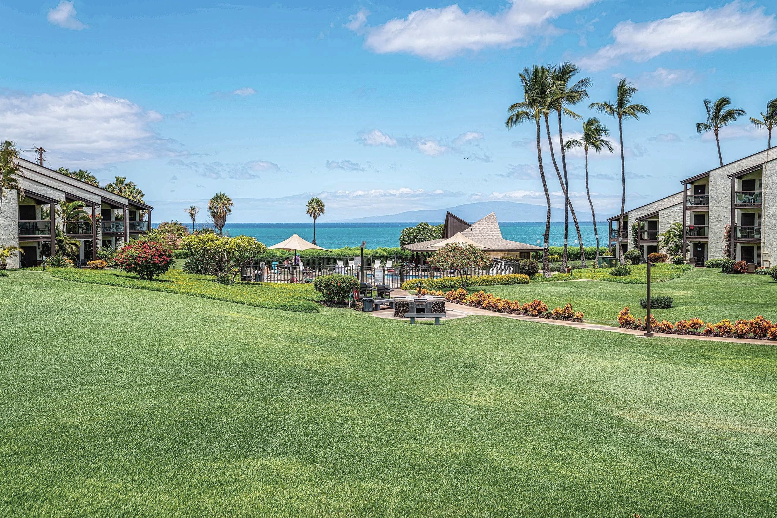 A resort with multiple buildings, a well-maintained lawn, and a view of the ocean.