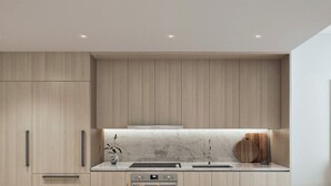 A modern kitchen with light wood cabinetry, a marble countertop, and built-in appliances. - NEW amenity-rich studio near Hard rock Stadium by SLS & ICON developers (Miami)