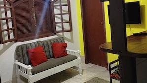 Quarto com sofá, tapete pequeno, porta de madeira e TV fixada na parede.