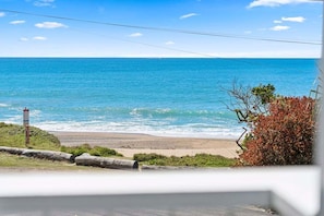 A coastal view with a sandy beach, a clear blue sky, and a signpost in the foreground. - Miss Beachy – Stunning Beachfront Home, Pet Friendly, Amazing Views (Sapphire Beach)