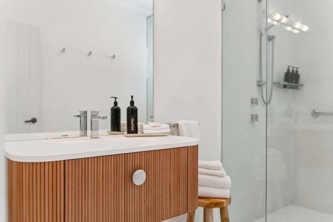 A modern bathroom with a wooden vanity, a large mirror, and a glass shower enclosure.