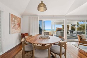 A dining area with a wooden table and chairs, a decorative centerpiece, and a view of the outdoors. - Miss Beachy – Stunning Beachfront Home, Pet Friendly, Amazing Views (Sapphire Beach)