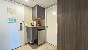 Ett litet, praktiskt kök med kylskåp, kaffebryggare och en papperskorg.