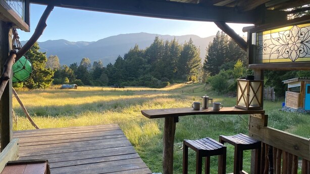 Une terrasse en bois offrant une vue sur un champ verdoyant et des montagnes au loin.