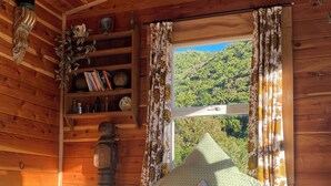 Une pièce de style cabane en bois, avec un lit, des oreillers, une étagère avec des livres et une bouteille, et une fenêtre avec des rideaux.
