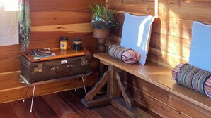 L’intérieur d’un chalet en bois, avec un banc, une valise, un panier suspendu et une plante en pot.