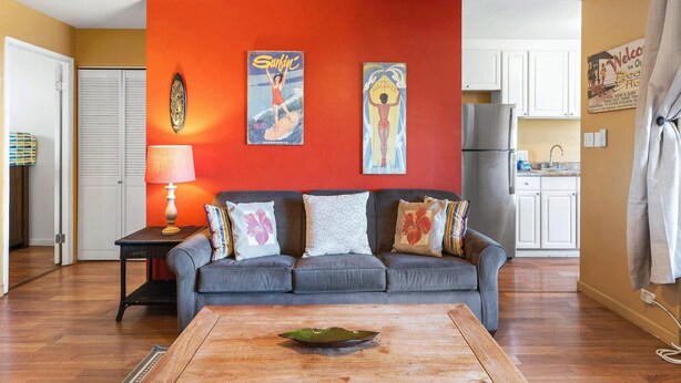 A living room with a grey sofa, a wooden coffee table, and a red accent wall. - Kalama Terrace P-307 - 3rd-floor Walkup, 7 min Walk to Charley Young Beach, AC! (Kihei)