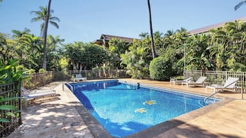 Una piscina rectangular con superficie de agua azul cristalina, rodeada por una plataforma de hormigón. Hay tumbonas y una valla metálica alrededor de la piscina.