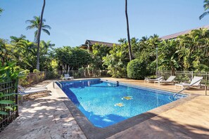 Una piscina rectangular con superficie de agua azul cristalina, rodeada por una plataforma de hormigón. Hay tumbonas y una valla metálica alrededor de la piscina.