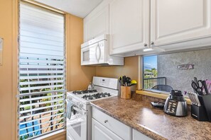 Une cuisine équipée d’une cuisinière à gaz, d’un four à micro-ondes et d’une fenêtre avec des stores.