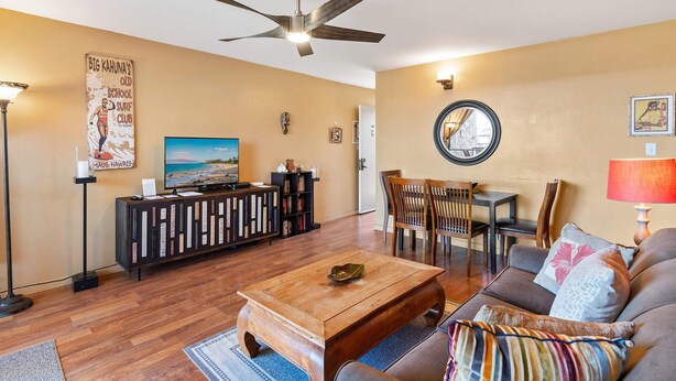 A living room with a ceiling fan, a television, a coffee table, a sofa, and a dining area with chairs and a table. - Kalama Terrace P-307 - 3rd-floor Walkup, 7 min Walk to Charley Young Beach, AC! (Kihei)