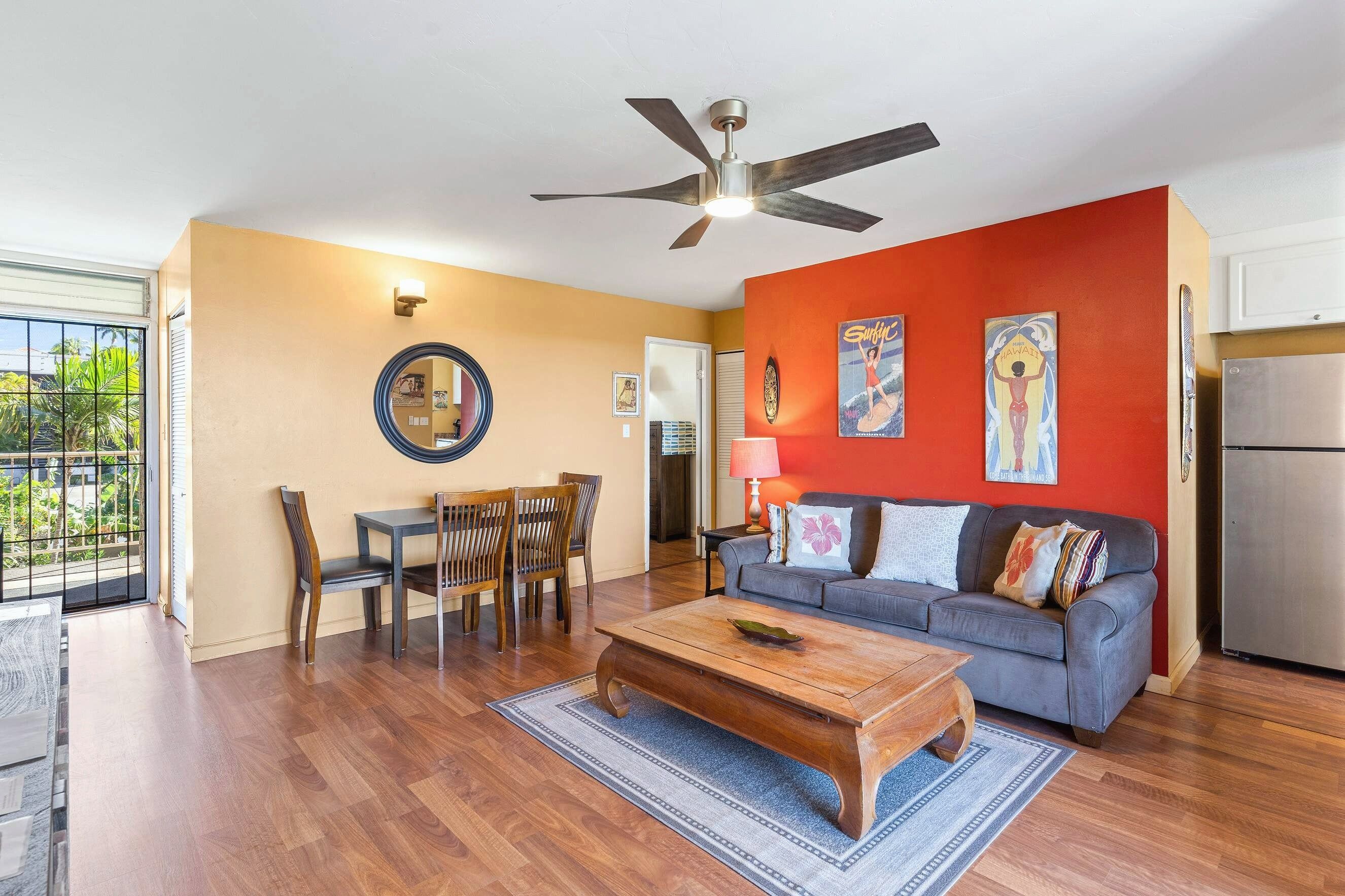 A living room with a ceiling fan, a gray sofa with decorative pillows, a wooden coffee table, and a dining area with chairs and a table.