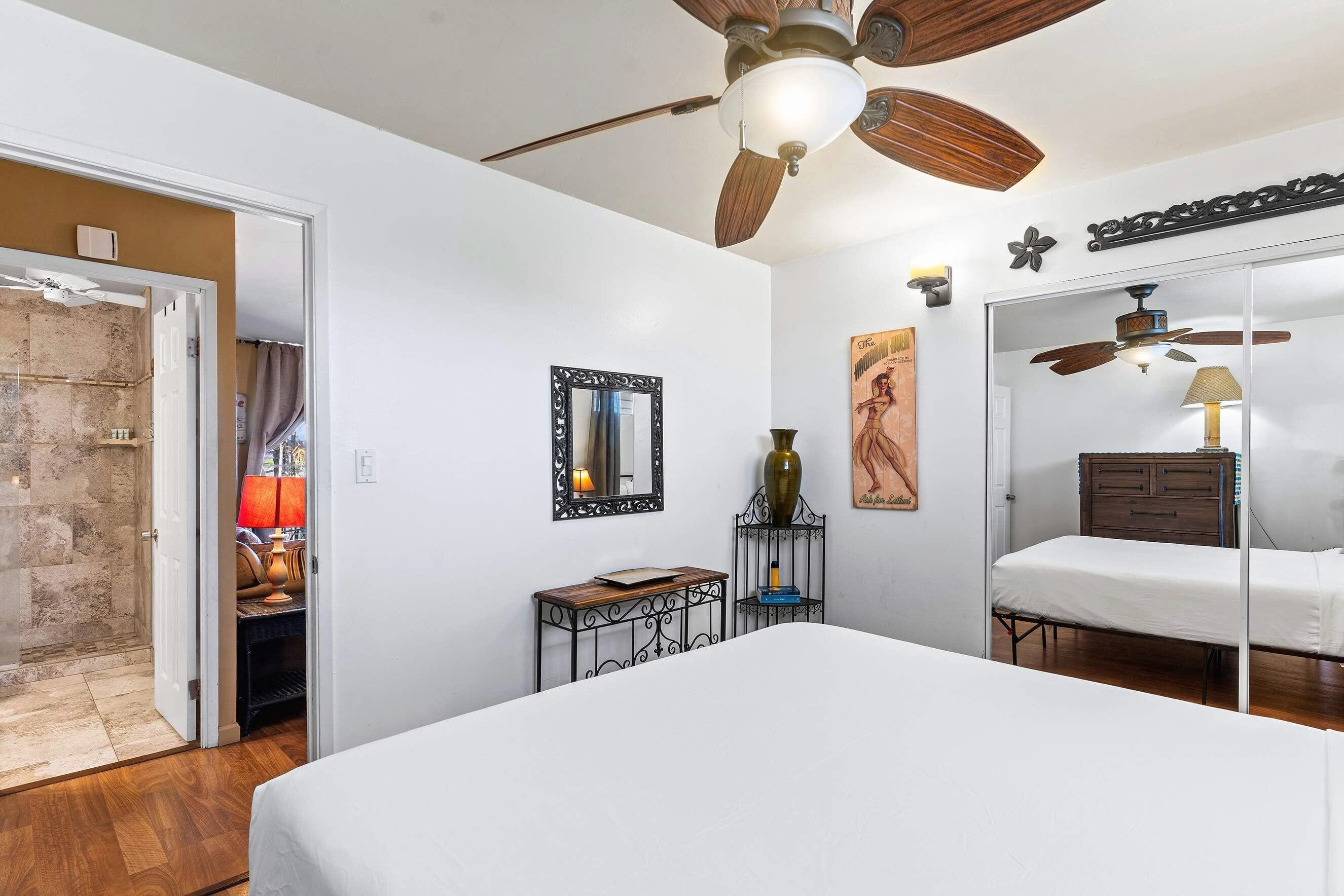 Quarto com cama, ventilador de teto, espelho, mesinha e cômoda.