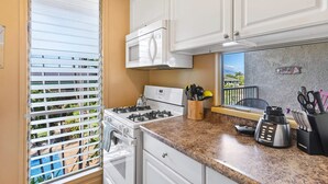A kitchen with a gas stove, a microwave, and a window with blinds. - Kalama Terrace P-307 - 3rd-floor Walkup, 7 min Walk to Charley Young Beach, AC! (Kihei)