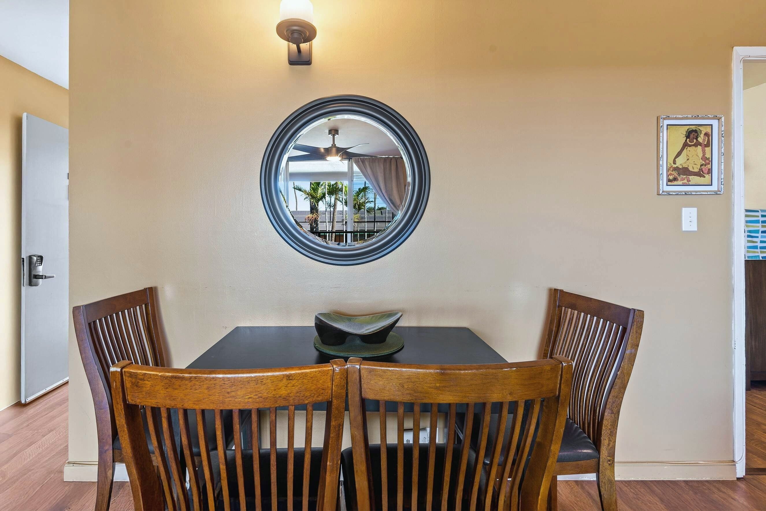 A dining area with a round mirror, two wooden chairs, a table, and a ceiling fan.