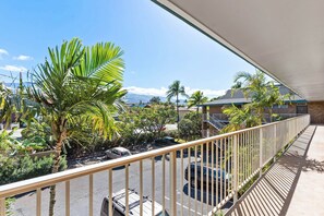 A balcony with a view of a parking area, palm trees, and a building with a sloped roof. - Kalama Terrace P-307 - 3rd-floor Walkup, 7 min Walk to Charley Young Beach, AC! (Kihei)