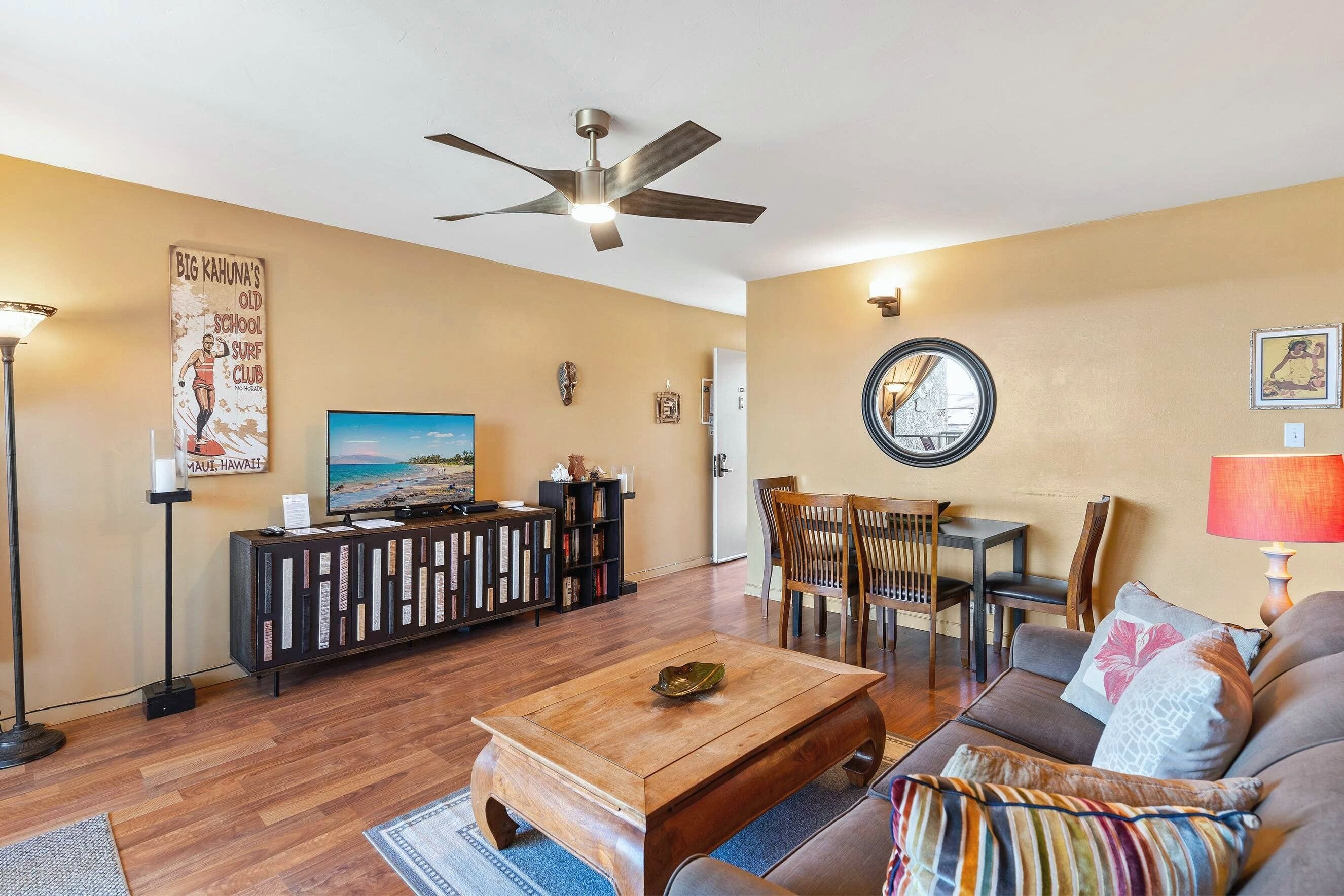 A living room with a ceiling fan, a television, a coffee table, a sofa, and a dining area with chairs and a table.