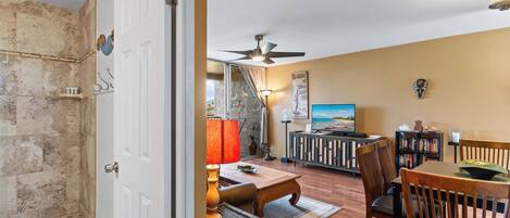 A living room with a dining area, a ceiling fan, a television, and a wall-mounted artwork.