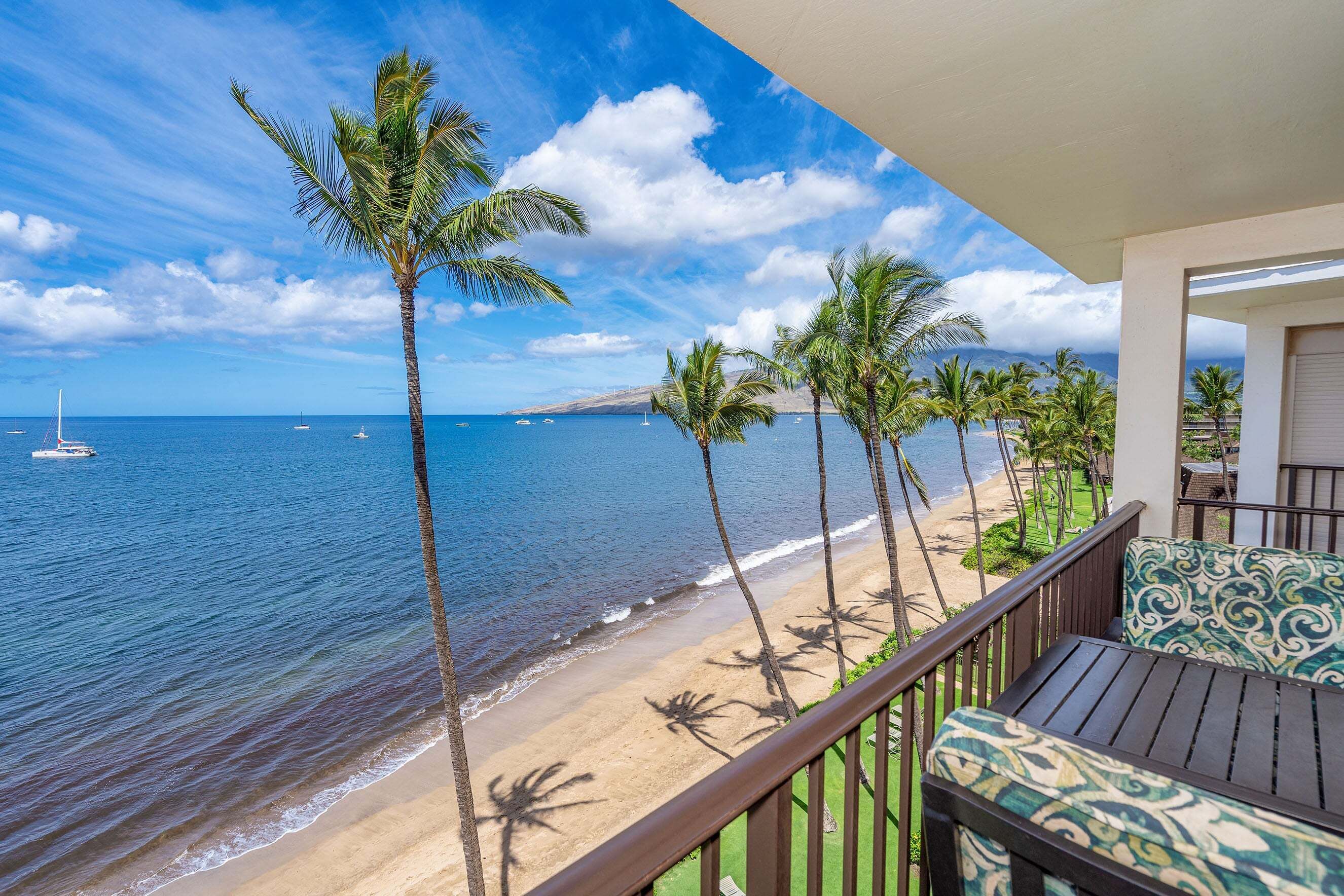 A balcony with a view of a beach and ocean, featuring palm trees and a clear sky.