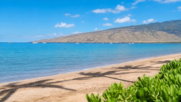 Egy tiszta, kék vízzel rendelkező strand, homokos parttal és a távolban elterülő hegyvonulattal.