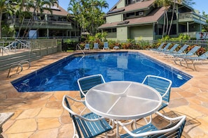 Ein Swimmingpool mit Liegestühlen und einem Tisch, umgeben von einer Steinterrasse und tropischen Pflanzen.
