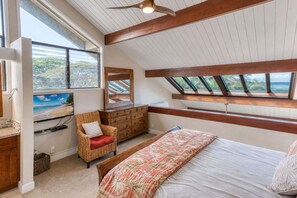 Ein Schlafzimmer mit Bett, Kommode, Sessel, Fernseher und Oberlicht.