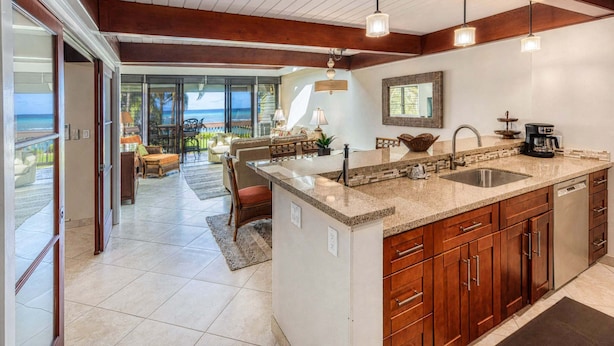 A modern kitchen with a large island, wooden cabinets, and a view to the outdoors. - Kahana Outrigger 4B1 - Breathtaking Ocean Views, Renovated Condo, Secluded Beach (Lahaina)