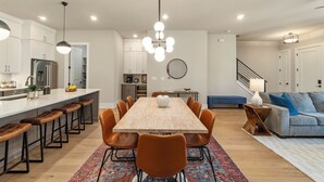 Una cocina moderna con armarios blancos, una isla grande con taburetes, una mesa de comedor con sillas y una escalera que sube a otro nivel.
