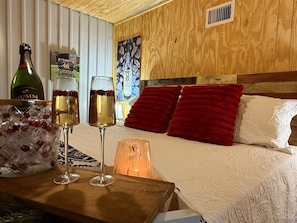 A room with a bed, two glasses of wine, a bottle of wine, and a decorative wall piece.