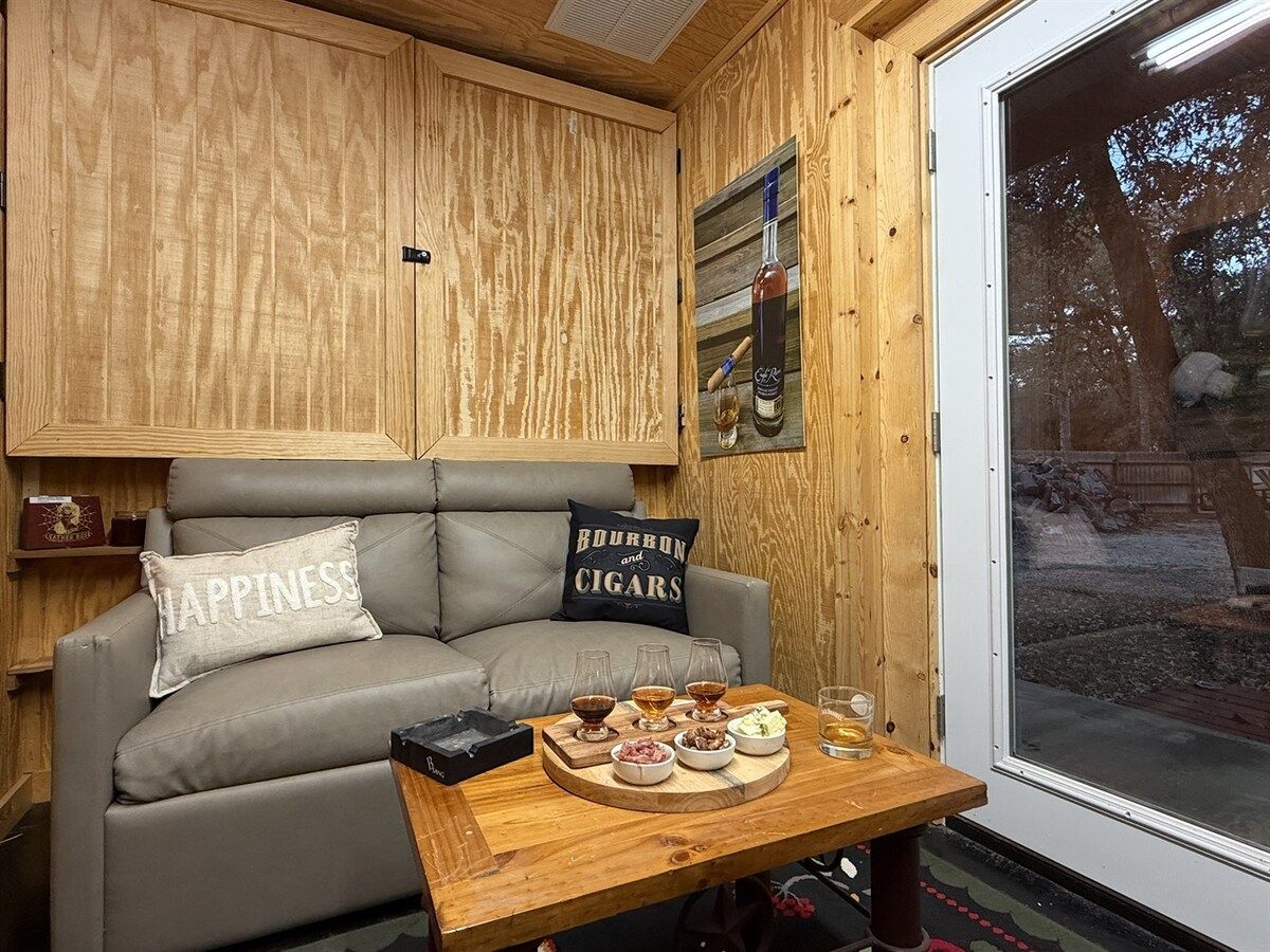 A cozy room with a grey sofa, a wooden table with a tray of food and drinks, and a window with a view of the outdoors.