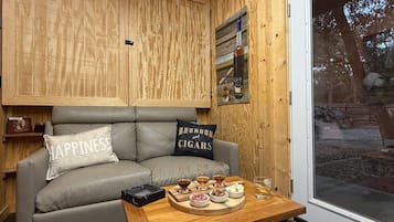 A cozy room with a grey sofa, a wooden table with a tray of food and drinks, and a window with a view of the outdoors.