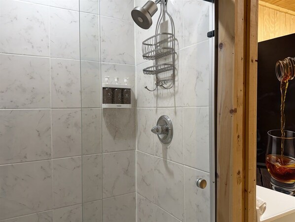 A bathroom with a shower, a towel rack, and a glass of whiskey on the counter.