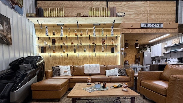 Un salon chaleureux avec des canapés en cuir, une table basse et une étagère murale où sont exposées différentes bouteilles.